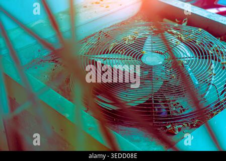 An abandoned cooling unit showcases a dusty fan covered in leaves, set against a vibrant blue backdrop. The image captures the essence of neglect and Stock Photo