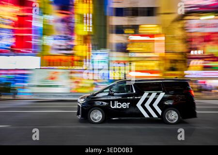 Uber taxi cab drives at high speed at Akihabara Electric Town district brightly illuminated at night. Chiyoda City, Tokyo, Japan. Stock Photo