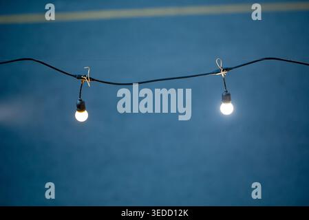 Two glowing bulbs hang from a wire, illuminating the night with a soft light. Perfect for summer gatherings or festive outdoor settings. Stock Photo