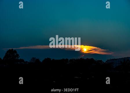 A serene sunset showcases a blend of warm orange and cool blue hues against a backdrop of clouds and distant trees, creating a tranquil outdoor scene. Stock Photo