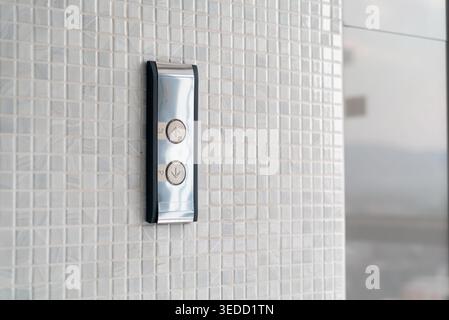 A close-up view of a modern elevator button panel mounted on a textured tile wall, showcasing sleek design and technology in an urban setting. Stock Photo