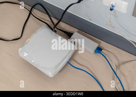 A modern wireless router connected to power and other cables on a wooden surface, designed for optimal internet connectivity at home or office. Stock Photo