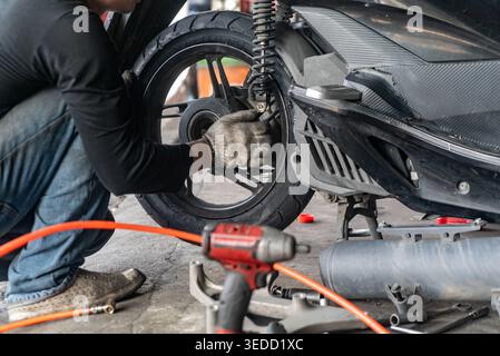 A mechanic performs maintenance on a scooter in a workshop, focusing on the suspension system. The scene showcases tools and parts involved in the rep Stock Photo