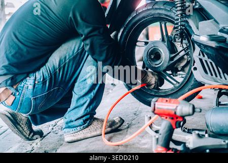 A mechanic performs tire repair on a motorcycle in a workshop. The focus is on the hands at work, using tools for maintenance and repair tasks. Stock Photo