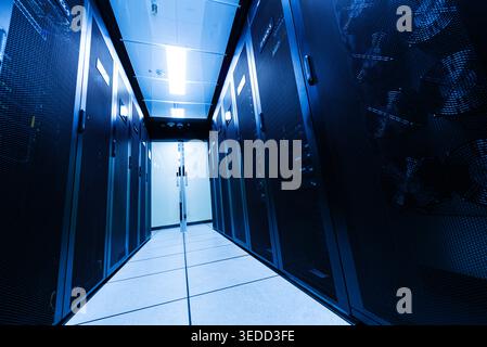 An interior view of a dark server room featuring blue lighting and rows of server racks, showcasing modern technology and data storage infrastructure. Stock Photo