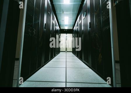 Narrow aisle in a server room filled with dark storage cabinets and network cables. The modern setup emphasizes technological infrastructure and organ Stock Photo