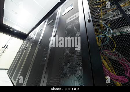This image shows a server room filled with network equipment, featuring well-organized server racks, cables, and cooling fans in a modern technologica Stock Photo