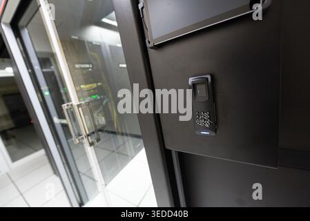 This image showcases a secure access control system at a data center, featuring a biometric fingerprint scanner next to a modern glass door entrance. Stock Photo