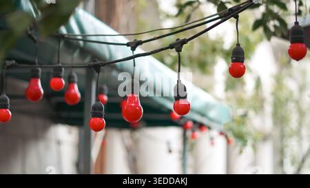 Horizontal photo of red decorative light bulbs hanging on a string outdoors. Stock Photo