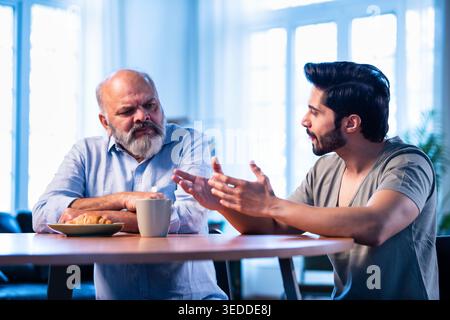 Indian young son having serious conversation with senior father in modern living room at home, emotional family discussion between two generations sha Stock Photo