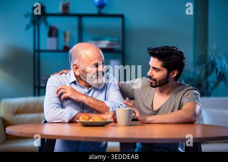 Indian young son having serious conversation with senior father in modern living room at home, emotional family discussion between two generations sha Stock Photo