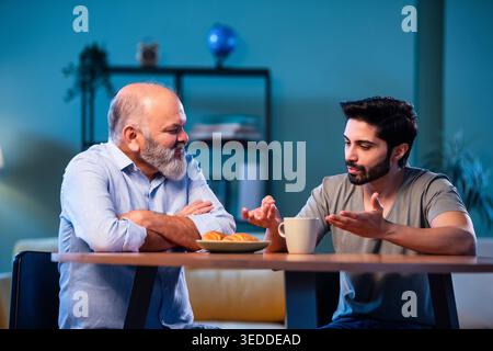 Indian young son having serious conversation with senior father in modern living room at home, emotional family discussion between two generations sha Stock Photo