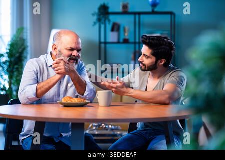 Indian young son having serious conversation with senior father in modern living room at home, emotional family discussion between two generations sha Stock Photo