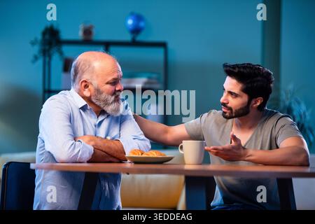 Indian young son having serious conversation with senior father in modern living room at home, emotional family discussion between two generations sha Stock Photo