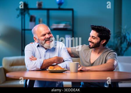 Indian young son having serious conversation with senior father in modern living room at home, emotional family discussion between two generations sha Stock Photo