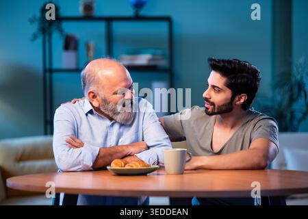 Indian young son having serious conversation with senior father in modern living room at home, emotional family discussion between two generations sha Stock Photo