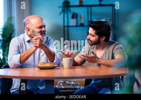 Indian young son having serious conversation with senior father in modern living room at home, emotional family discussion between two generations sha Stock Photo