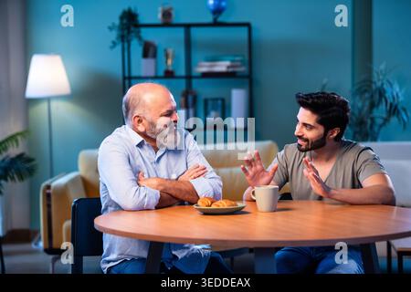 Indian young son having serious conversation with senior father in modern living room at home, emotional family discussion between two generations sha Stock Photo
