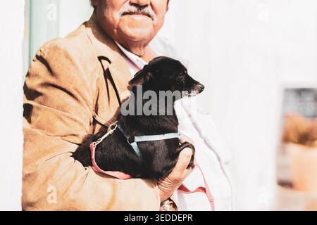 Elderly senior man with a mustache holding his small black dog outdoors Stock Photo