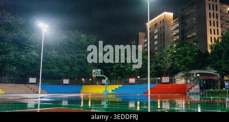 Nighttime basketball court with colorful bleachers, wet reflective surface under stadium lights, Stock Photo