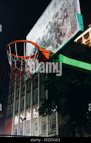 Nighttime low-angle shot of a weathered basketball hoop with orange rim and red net, mounted on Stock Photo
