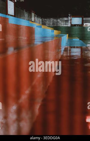 Wet colorful stadium bleachers reflecting in rainwater pool, low-angle perspective with vibrant red Stock Photo