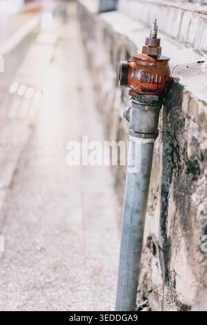Weathered red fire hydrant mounted on concrete wall beside paved alleyway, shallow depth of field, Stock Photo