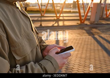 Hands Holding a Smartphone During Golden Hour with Sun Flare Background Stock Photo