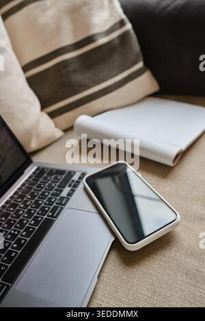 Laptop, smartphone, and open blank notebook on a cozy sofa during remote work at home Stock Photo