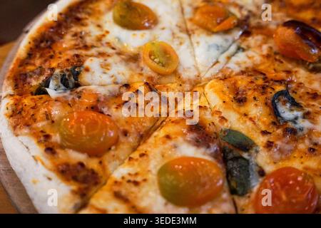 Freshly baked pizza with cherry tomatoes, basil, and melted cheese on wooden board. Stock Photo