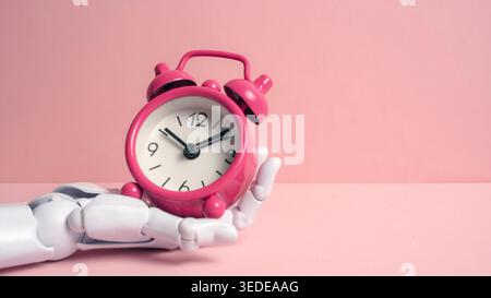 Description: White robotic hand holding a pink vintage alarm clock against a pastel pink background representing AI time management and future technol Stock Photo