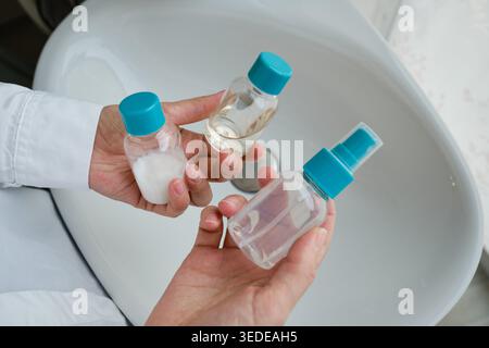 Person in a white shirt holding two small clear plastic bottles with blue caps on their palms Stock Photo