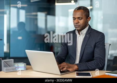African american businessman focused on his work while typing on a laptop computer at a desk in a contemporary corporate office environment, representing professionalism and productivity Stock Photo