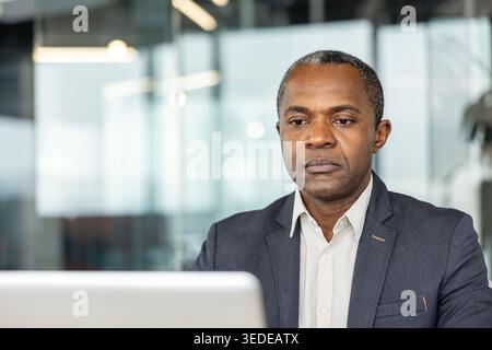 Mature professional businessman in a smart suit concentrating on a laptop in a modern office, deeply focused on work and strategic decision-making with a serious expression Stock Photo