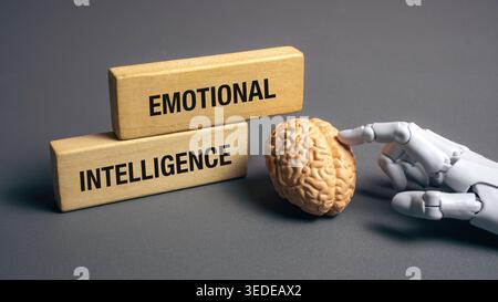 Robot hand touching a human brain model next to emotional intelligence wooden blocks on a grey background representing advanced AI and empathy. Stock Photo