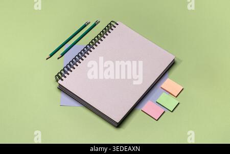 A notebook is placed on a flat green surface along with two colored pencils and several sticky notes. The items are neatly organized for writing and n Stock Photo
