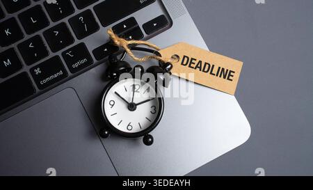 Deadline Tag on Small Black Alarm Clock Placed on Laptop Keyboard Representing Work Pressure and Time Constraints Stock Photo
