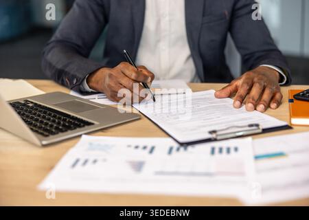 Entrepreneur signing a business contract, focusing on legal paperwork at a modern office desk with a laptop and financial documents, symbolizing agreement, success, and official procedures Stock Photo