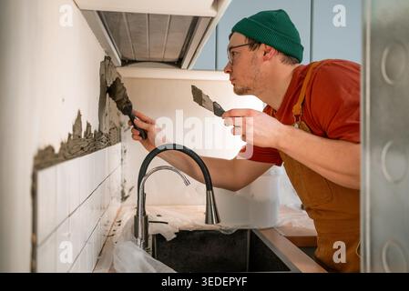 Tiler applying adhesive mortar to a kitchen wall for installing new ceramic tiles, preparing the surface for a modern backsplash during a home renovation project Stock Photo