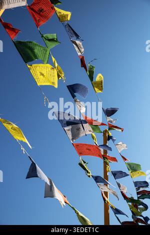 Tibetan prayer flags are hanging on lines, moving gently in the breeze. They are displayed at a Buddhist temple during a sunny day, creating a colorfu Stock Photo