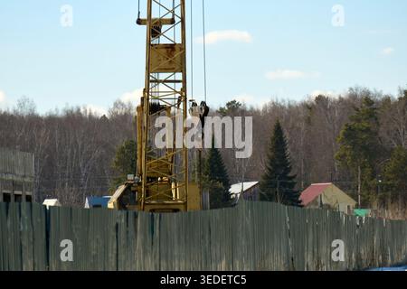 Construction cranes lift heavy materials at a building site in daylight with a clear sky and clouds overhead Stock Photo