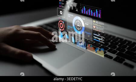 A hand interacts with a laptop screen displaying futuristic data visualizations. Graphs and interactive elements showcase technology and information Stock Photo