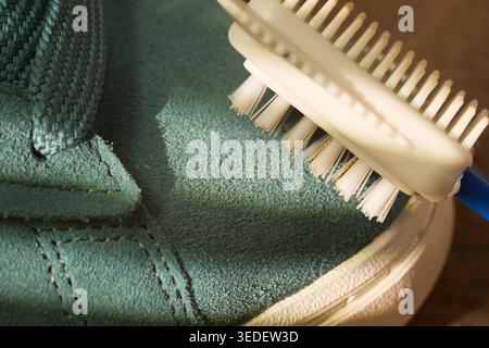 bristle cleaner extracting dirt from sneaker seam, handheld demo shows white head and blue handle sweeping debris, textured suede background Stock Photo