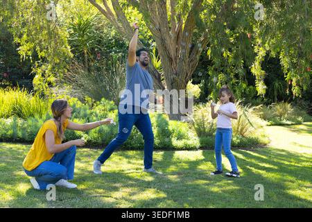 Diverse family playing with bubble wands and soap bubbles on grassy lawn under large shade tree Stock Photo