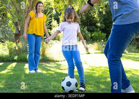 Diverse family playing soccer in backyard, child girl preparing to kick soccer ball, wristwatch Stock Photo