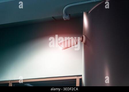 A modern surveillance camera mounted on a sleek wall, featuring a warning light, emphasizing security and monitoring in urban environments. Stock Photo