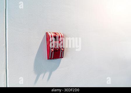 A red fire alarm box mounted on a white wall, designed for emergency situations. The device serves as a critical safety alert tool within various buil Stock Photo