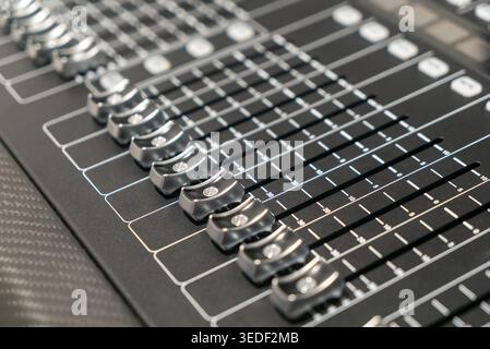 Close-up view of a professional audio mixing console showcasing various controls, sliders, and knobs used in sound production and music engineering. Stock Photo
