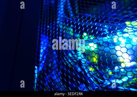 A close-up view of colorful LED lights shining through a metal mesh, creating a dynamic and futuristic atmosphere. The blend of blue and green hues of Stock Photo