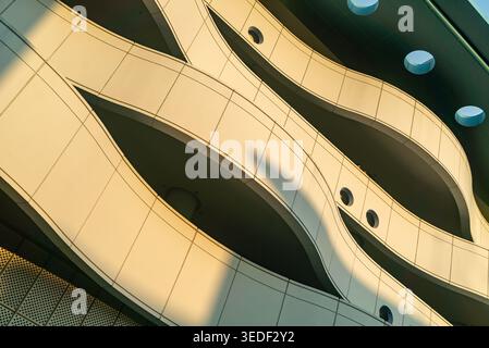 This image captures the elegant lines and curves of a modern building facade, showcasing unique architectural design under soft sunlight and shadow pl Stock Photo